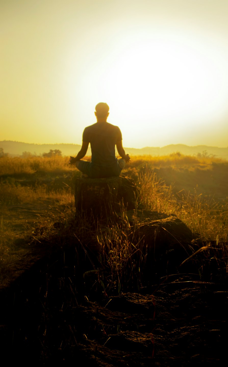 Person meditating on a rock at sunset.